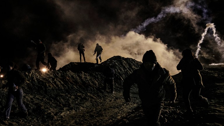 Migrants run as tear gas is thrown by U.S. Border Protection officers to the Mexican side of the border fence after they climbed the fence to get to San Diego, Calif.