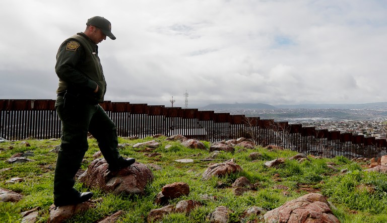 An officer on the American side of the U.S.-Mexico border walks near a wall.