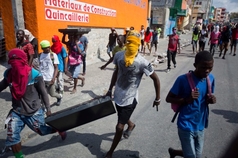 Masked looters carry a flat screen TV amid protests demanding the resignation of Haitian President Jovenel Moise near the presidential palace in Port-au-Prince, Haiti, Wednesday, Feb. 13, 2019. Protesters are angry about skyrocketing inflation and the government's failure to prosecute embezzlement from a multi-billion Venezuelan program that sent discounted oil to Haiti. 