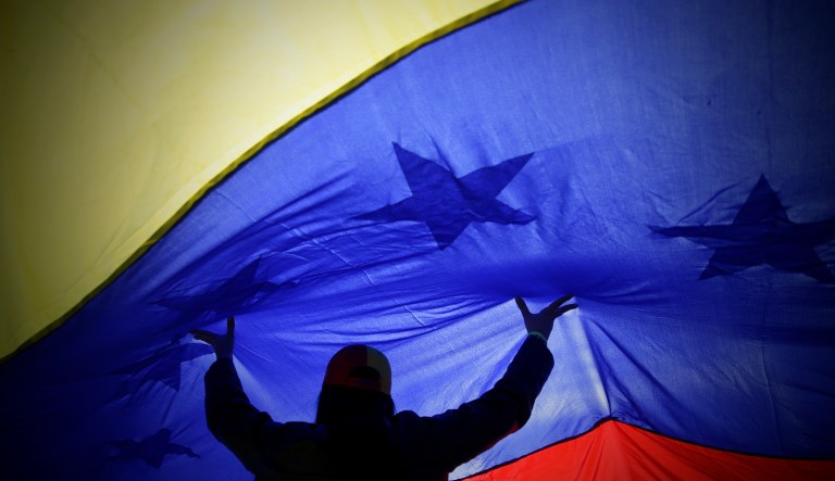 A woman lifts up a big Venezuelan flag during a rally.