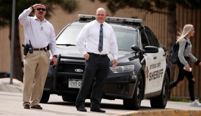 Columbine High School principal Scott Christy, right, joins an officer in watching as students leave the school late Tuesday, April 16, 2019, in Littleton, Colo. Following a lockdown at Columbine High School and other Denver area schools, authorities say they are looking for a woman suspected of making threats.