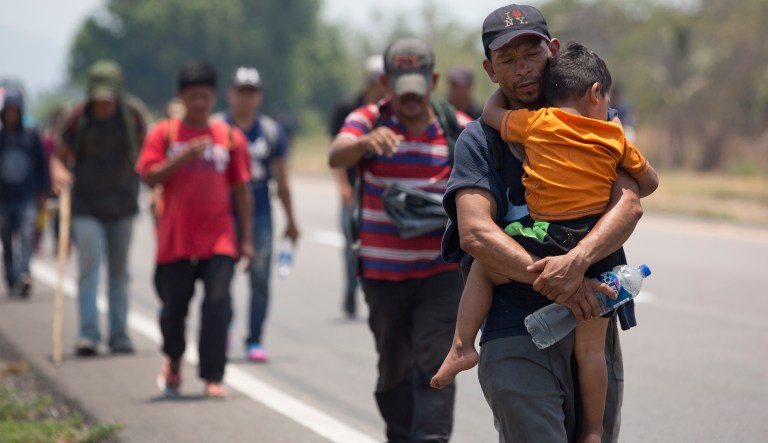 A Central American migrant man carrying a child walks along the highway in Mexico.