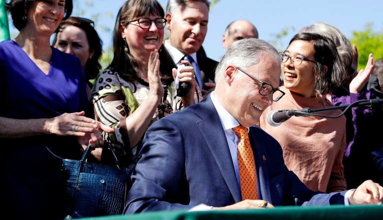Washington Gov. Jay Inslee, seated right, is applauded as he signs a bill addressing climate change on Tuesday in Seattle.