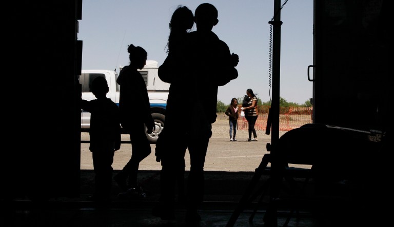 In this Wednesday, May 22, 2019, migrants mainly from Central America guide their children through the entrance of a World War II-era bomber hanger in Deming, N.M. A surge of asylum-seeking families has been straining cities along the southern U.S. border for months, but now the issue is flowing into cities far from Mexico, where immigrants are being housed in an airplane hangar and rodeo fairgrounds and local authorities are struggling to keep up with the influx.