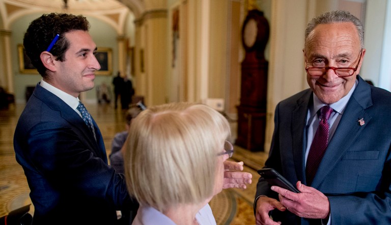 Senate Minority Leader Sen. Chuck Schumer of New York (right) smiles as an aide hands him another cellphone during a news conference.