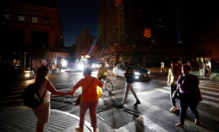 Pedestrians cross a dark street during a power outage, Saturday, July 13, 2019, in New York. 