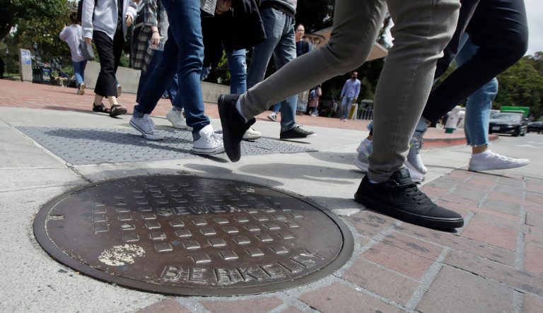 Pedestrians walk past a manhole cover for a sewer in Berkeley, Calif., Thursday, July 18, 2019. 