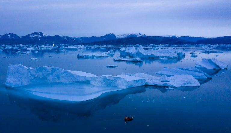 In this Aug. 15, 2019, photo, a boat navigates at night next to large icebergs near the town of Kulusuk, in eastern Greenland. 