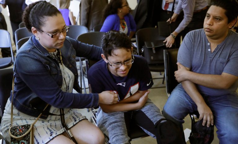 Gary Sanchez, of Honduras, right, watches as his wife, Mariela comforts their son, Jonathan, 16, during a news conference, Monday, Aug. 26, 2019, in Boston. The Sanchez family came to the United States seeking treatment for Jonathan's cystic fibrosis. Doctors and immigrant advocates say federal immigration authorities are unfairly ordering foreign born children granted deferred action for medical treatment to return to their countries. 