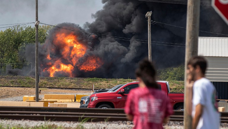 Onlookers stop in a parking lot across from a fire in the Dupo, Ill., train yard.