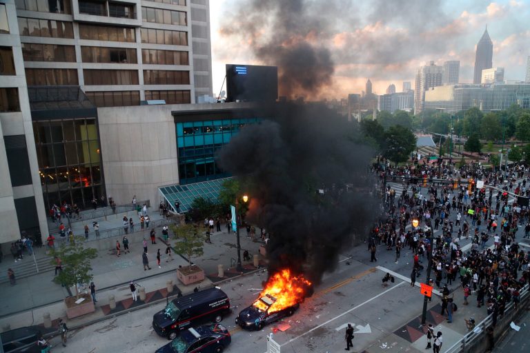 A police car burns after protesters marched to the Georgia State Capitol and returned to the area around the Centennial Olympic Park and CNN center where some confronted police Friday, May 29, 2020, in Atlanta. The protesters carried signs and chanted  messages of outrage over the death of George Floyd, a handcuffed back man who died Memorial Day in the custody of the Minneapolis police. 