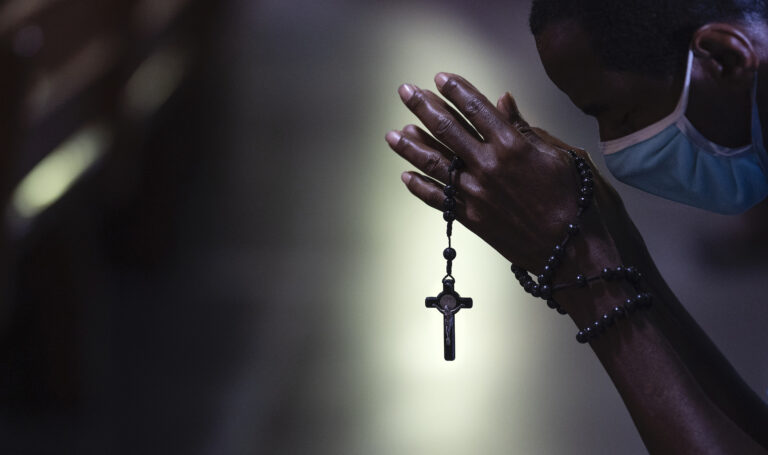 With rosary beads wrapped around clasped hands, a man bows in prayer during a Mass at the Metropolitan Cathedral, in Rio de Janeiro, Brazil, Saturday, July 4, 2020. Following an easing of restrictions related to COVID-19, the Catholic church in Rio celebrated its first Mass with 30% of its worshippers, while observing preventive measures to avoid spreading the new coronavirus. (AP Photo/Leo Correa)