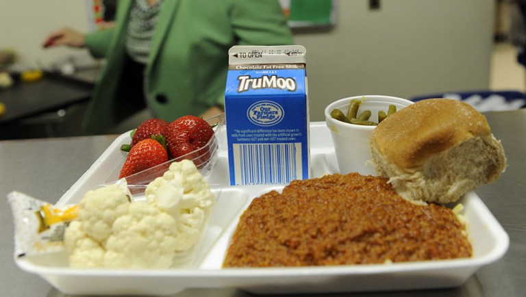 Becky Domokos-Bays, the Director of Food and Nutrition Services at Alexandria City Public Schools, holds up a tray of food during lunch service.