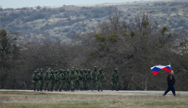 Russian soldiers walk as a local resident waves with a Russian flag outside of a Ukrainian military base in the village of Perevalne, outside of Simferopol, Crimea, in 2014.
