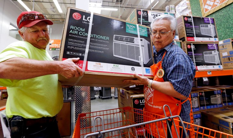 In this Tuesday, Aug. 1, 2017, file photo, store greeter Danny Olivar, right, lends a hand to a customer, who declined to be identified, to heft an air conditioning unit from a rapidly declining stock at a Home Depot store ahead of an expected heat wave in Seattle. The Home Depot Inc. reports earnings Tuesday, Aug. 15, 2017. 