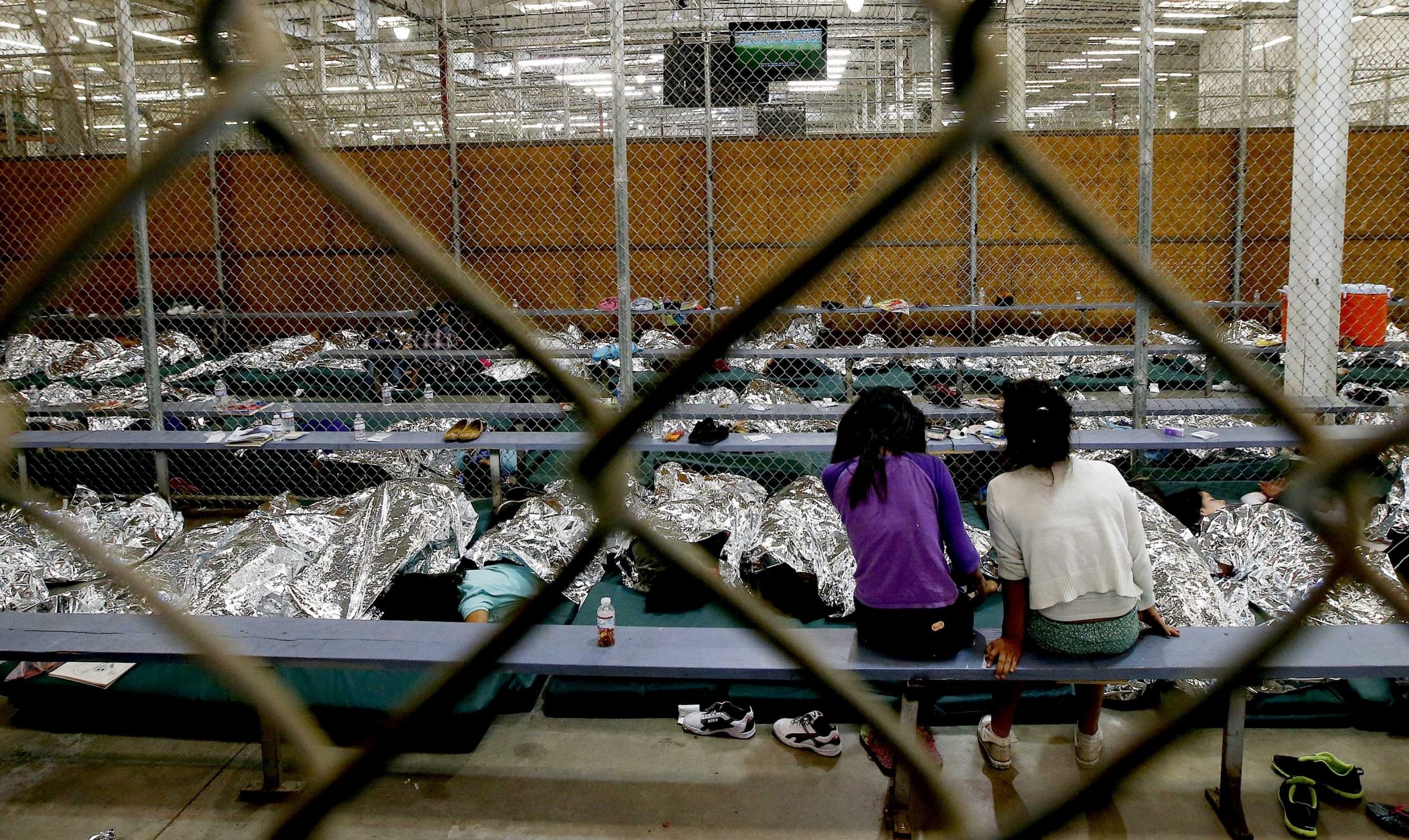 In this June 18, 2014, photo, two young girls watch a World Cup soccer match on a television from their holding area where hundreds of mostly Central American immigrant children are being processed and held at the U.S. Customs and Border Protection Nogales Placement Center in Nogales, Arizona.