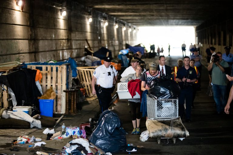 A couple, center, who were living under a bridge carry their possessions out as police move in to clear the encampment in Philadelphia, Wednesday, May 30, 2018. The cityâs homeless packed up their few belongings as sanitation workers cleaned and power washed what had been a heroin encampment only moments before. The morning activity attended by police was part of a monthlong pilot program meant to relocate addicts living under two bridges in Philadelphia.