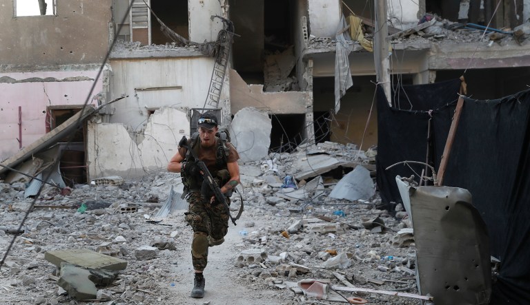 In this July 27, 2017 file photo, a U.S.-backed Syrian Democratic Forces fighter runs in front of a damaged building as he crosses a street on the front line, in Raqqa, Syria. Syrian activists said Friday, Dec. 14, 2018 that U.S.-backed, Kurdish-led fighters have captured the last town held by the Islamic State group, in the militants' single remaining enclave in eastern Syria.