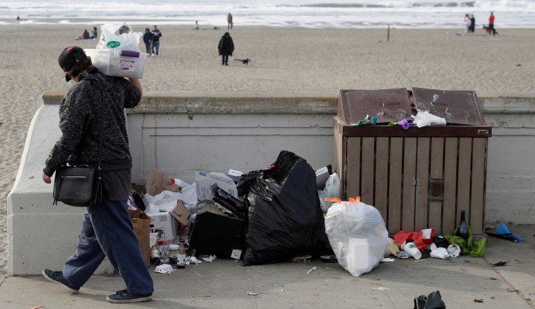 A woman walks past trash piled next to a garbage bin at Ocean Beach in San Francisco, Thursday, Jan. 3, 2019. Nonprofits, businesses and state governments across the country are paying bills and putting in volunteer hours in an uphill battle to keep national parks safe and clean for visitors as the partial U.S. government shutdown lingers.