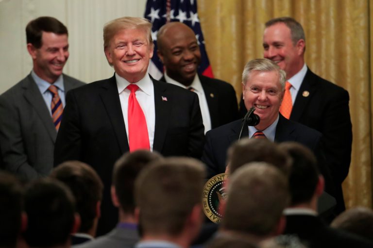 Sen. Lindsey Graham (R-SC) (front right) stands next to then-President Donald Trump during a 2019 ceremony welcoming the 2018 college football playoff National Champion Clemson Tigers to the White House.