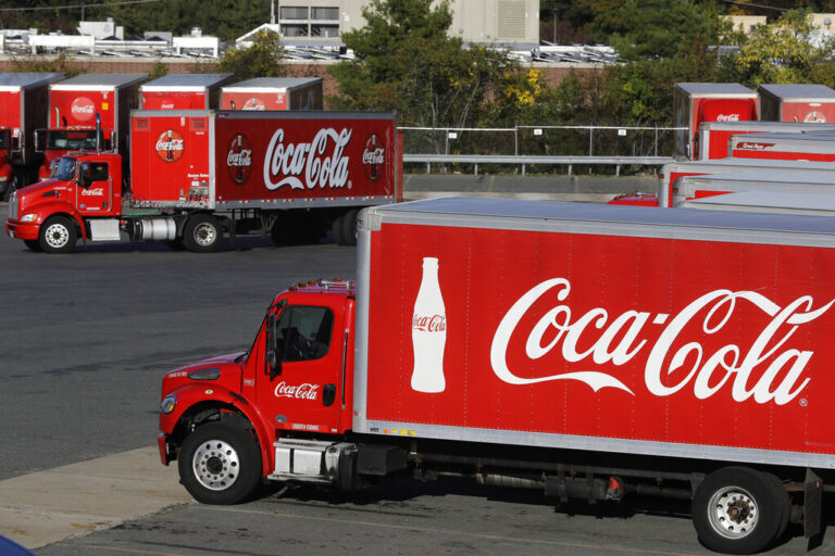FILE - In this Oct. 14, 2019 photo a truck with the Coca-Cola logo, behind left, maneuvers in a parking lot at a bottling plant in Needham, Mass. The Coca-Cola Co. reports financial results on Thursday, Jan. 30, 2020. 