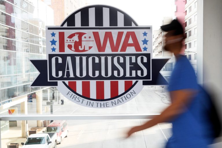 A pedestrian walks past a sign for the Iowa caucuses.