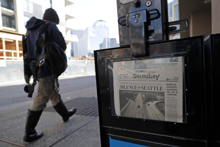 A man walks near a Seattle Times newspaper box in front of the building that houses the Times' newsroom, Sunday, March 15, 2020 in Seattle.