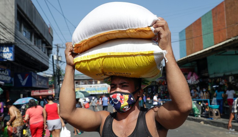 A worker, wearing a protective mask, carries sacks of rice before the Munoz market closes for it's morning business as they cut their operations to four hours a day as part the enhanced community quarantine to prevent the spread of the new coronavirus in Metro Manila, Philippines on Thursday, March 19, 2020.