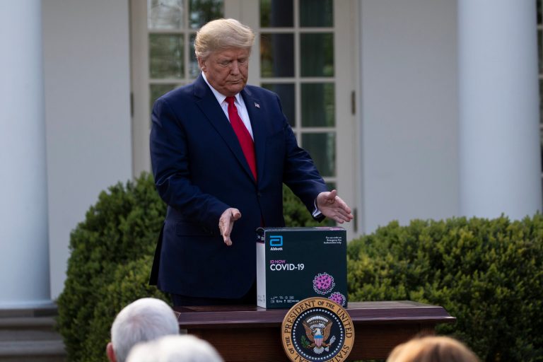 President Donald Trump reaches for a box containing a 5-minute test for COVID-19 from Abbott Laboratories, in the Rose Garden of the White House, Monday.
