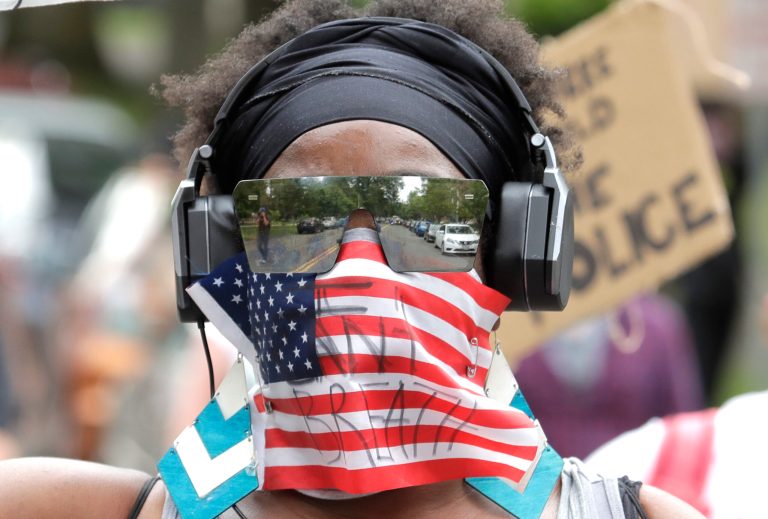 A person wears a flag that has "I can't breathe" written on it, Friday, June 5, 2020, in Tacoma, Wash., during a protest against police brutality and the death of George Floyd. A Gallup survey shows division over pride in America.