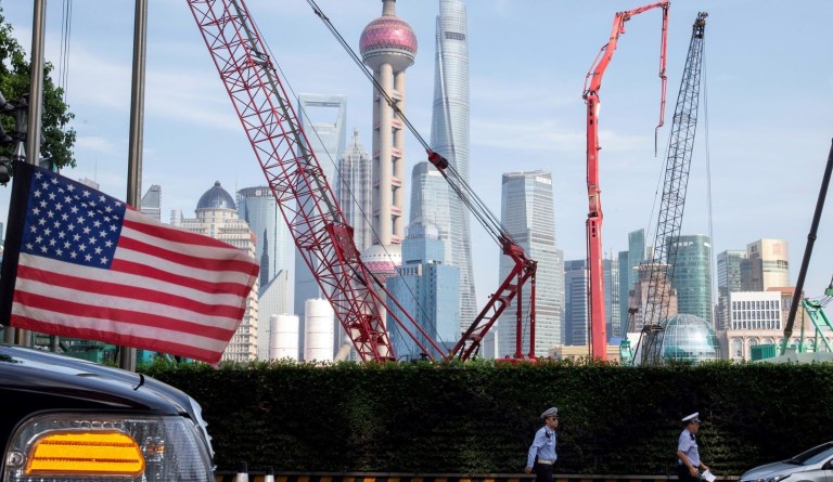 In this file photo taken Tuesday, July 30, 2019, Chinese traffic police officers walk by a U.S. flag on an embassy car outside a hotel in Shanghai where officials from both sides met for talks aimed at ending a tariff war. 