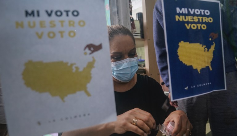 Salon owner Alejandra Moran tapes flyers to a door as part of a campaign to get voters to the polls by La Colmena, a community-based organization working with immigrant workers, in the largely Hispanic community of Port Richmond in Staten Island, N.Y., Friday, Oct. 23, 2020.