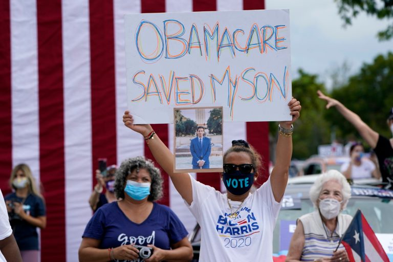 Adelys Ferro holds a sign in support of Obamacare as former President Barack Obama speaks while campaigning for Democratic presidential candidate former Vice President Joe Biden at Florida International University, Saturday, Oct. 24, 2020, in North Miami, Florida.