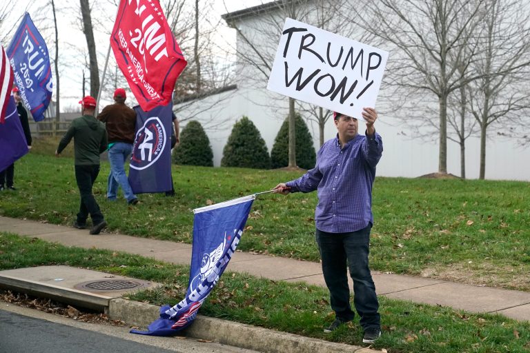 A supporter of President Donald Trump holds up a sign as Trump's motorcade departs Trump National Golf Club in Sterling, Va., Sunday, Dec. 13.
