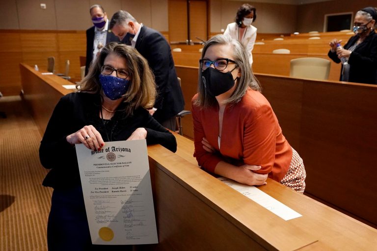 Arizona Electoral College member Felecia Rotellini, left, holds her commemorative Presidential Elector Ballot, as she poses for a photo with Arizona Secretary of State Katie Hobbs, right. The state has been targeted in several efforts to challenge the presidential vote.