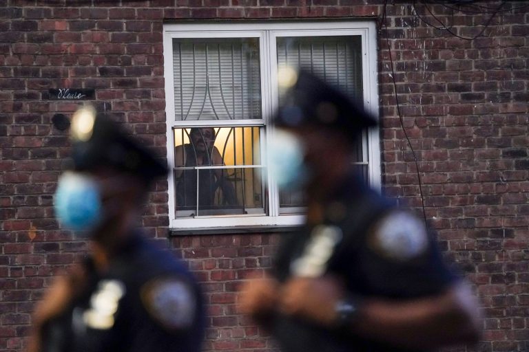 A neighbor watches New York City Police Department officers work a crime scene last August where several young men were shot and wounded at the Ravenswood Houses in the Queens borough of New York. Heralded as the safest big city in America in recent years, New York City is closing out its bloodiest year in nearly a decade, grappling with a surge in homicides and a pandemic authorities say has helped fuel violence.