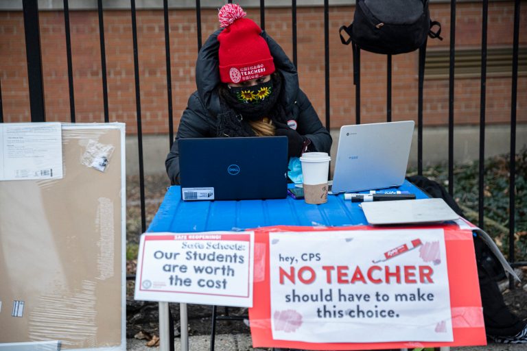 In this Monday, Jan. 11, 2021 file photo, elementary 1 teacher Melissa Vozar sits outside of Suder Elementary in Chicago to teach a virtual class. The Chicago Teachers Union said Sunday, Jan. 24 that its members voted to defy an order to return to the classroom before they are vaccinated against the coronavirus, setting up a showdown with district officials who have said such a move would amount to an illegal strike. 