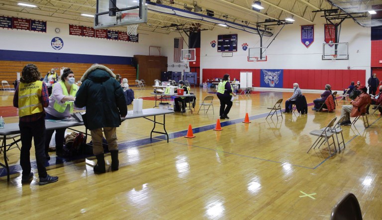 People wait for their turn to receive a COVID-19 vaccine, right, as public health experts with the Vermont Health Department begin vaccinating people aged 75 and older on Wednesday, Jan. 27, 2021, at the Hazen Union High School in Hardwick, Vt.