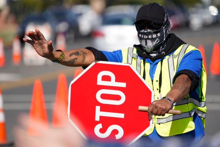Traffic controller Max Estrada stops drivers arriving without a face mask for a COVID-19 vaccine appointment at the mass vaccination site at the parking lot of L.A. County Office of Education headquarters in Downey, Calif., Wednesday. The virus is one reason Gallup said U.S. satisfaction is in the dumps.