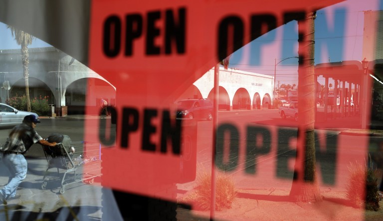  In this June 30, 2020, photo, a man passes a clothing shop with open signs in the window in Calexico, Calif.