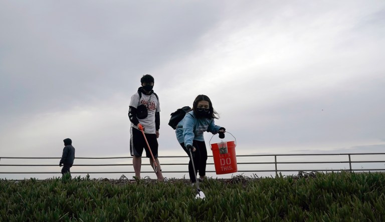 Pacifica Beach Coalition volunteers Alec Juntura, 21, foreground left, and Kimmy Tran, 20, clean trash near Sharp Park Beach in Pacifica, Calif., Wednesday, March 17, 2021.