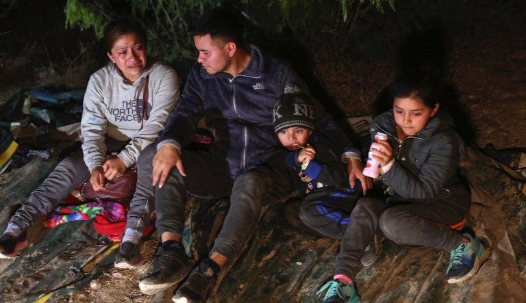 A family from Honduras sits on the ground after they were smuggled on an inflatable raft across the Rio Grande, in Roma, Texas Saturday, March 27, 2021. Roma, a town of 10,000 people with historic buildings and boarded-up storefronts in Texas' Rio Grande Valley, is the latest epicenter of illegal crossings, where growing numbers of families and children are entering the United States to seek asylum.