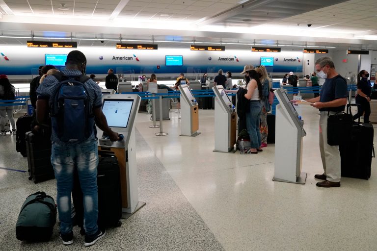 Travelers use the self-service kiosk to check in and pay for luggage at the American Airlines terminal, Thursday, April 29, 2021, in Miami.  Last year with the pandemic raging, travelers were urged to stay home. Not this year. With more people vaccinated, expect to see busier roads and airports as family and friends travel more. (AP Photo/Marta Lavandier)