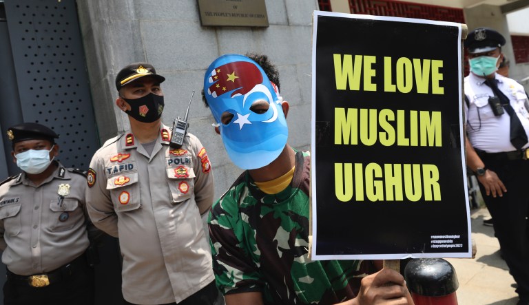 In this March 25, 2021, file photo, a Muslim student wearing a mask with the colors of the pro-independence East Turkistan flag, and the Chinese national flag in the shape of a hand holds a poster during a rally outside the Chinese Embassy calling for an end to alleged oppression of the Chinese Uyghurs in Jakarta, Indonesia.