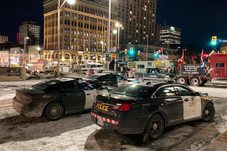 Police sit in cars by a convoy of trucks and other protesters in Ottawa, Ontario.