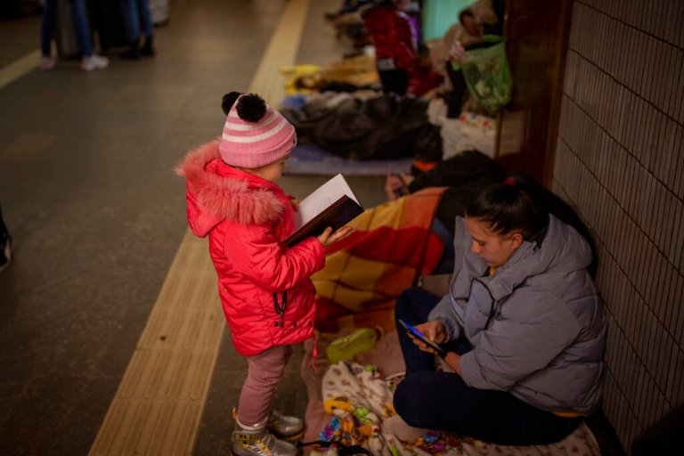 A girl looks at a notebook next to her mother as they stand in the Kyiv subway, using it as a bomb shelter, Ukraine, Saturday, Feb. 26, 2022.