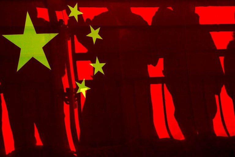 Spectators cast shadows on a Chinese national flag at a viewing platform during the men's and women's Alpine downhill at the 2022 Winter Paralympics, Saturday, March 5, 2022, in the Yanqing district of Beijing.