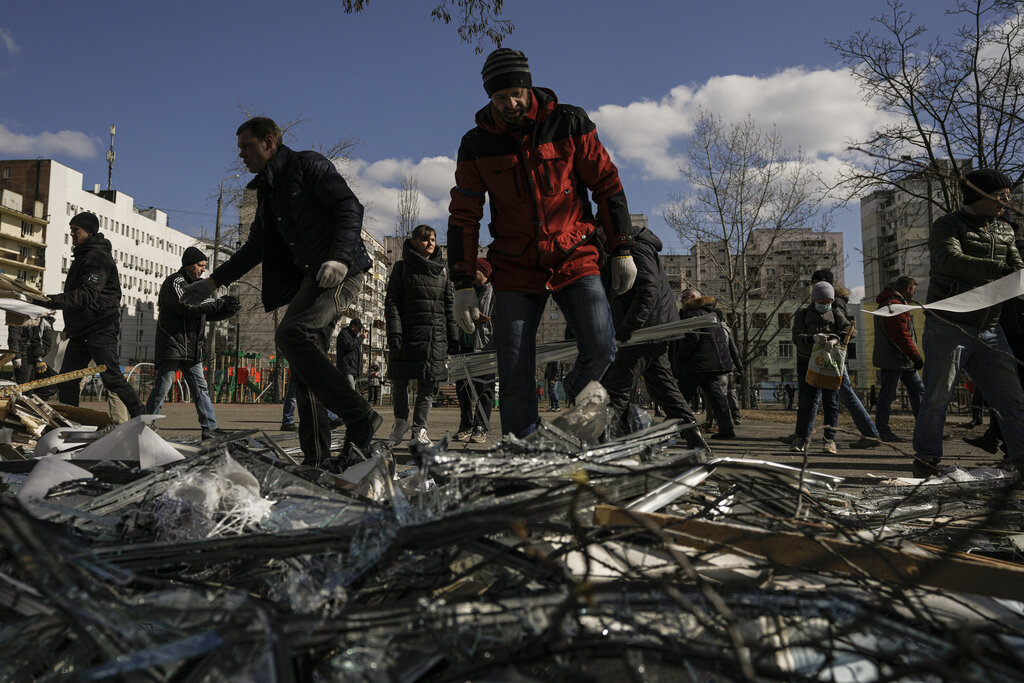 People clear debris outside a medical center damaged after parts of a Russian missile, shot down by Ukrainian air defense, landed on a nearby apartment block, according to authorities, in Kyiv, Ukraine, Thursday, March 17, 2022. Russian forces destroyed a theater in Mariupol where hundreds of people were sheltering Wednesday and rained fire on other cities, Ukrainian authorities said, even as the two sides projected optimism over efforts to negotiate an end to the fighting. 