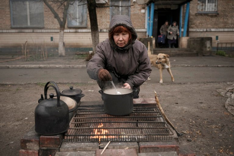 A woman cooks on an open fire outside an apartment building that, according to residents, has had no gas, water, electricity, and heating for more than a month in Bucha, Ukraine, on Saturday.