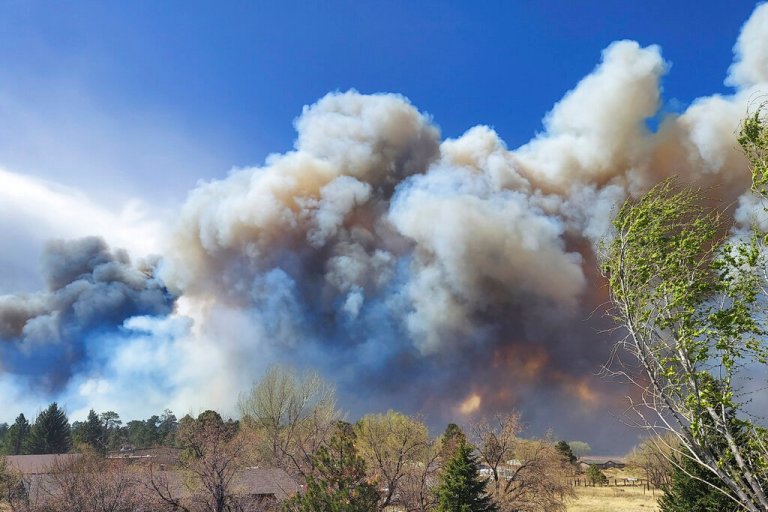 Smoke from a wind-whipped wildfire rises above neighborhoods on the outskirts of Flagstaff, Ariz., on Tuesday, April 19, 2022. Homes on the outskirts of Flagstaff were being evacuated Tuesday as high winds whipped a wildfire, shut down a major highway, and grounded firefighting aircraft.